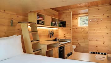 Una cabaña de madera compacta con kitchenette, una cama y un ventanal.