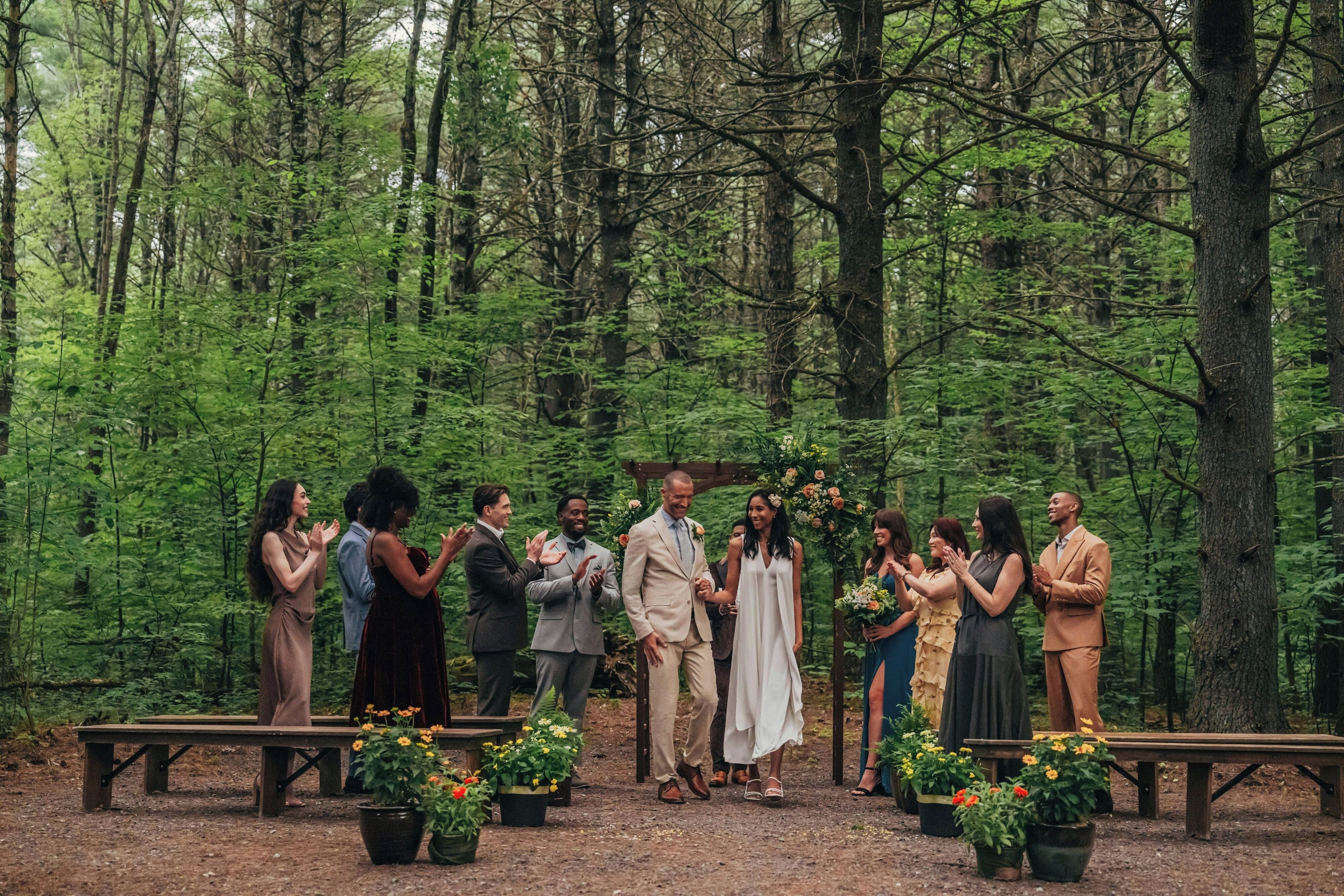 A group of people standing in a forested area with benches and potted plants.