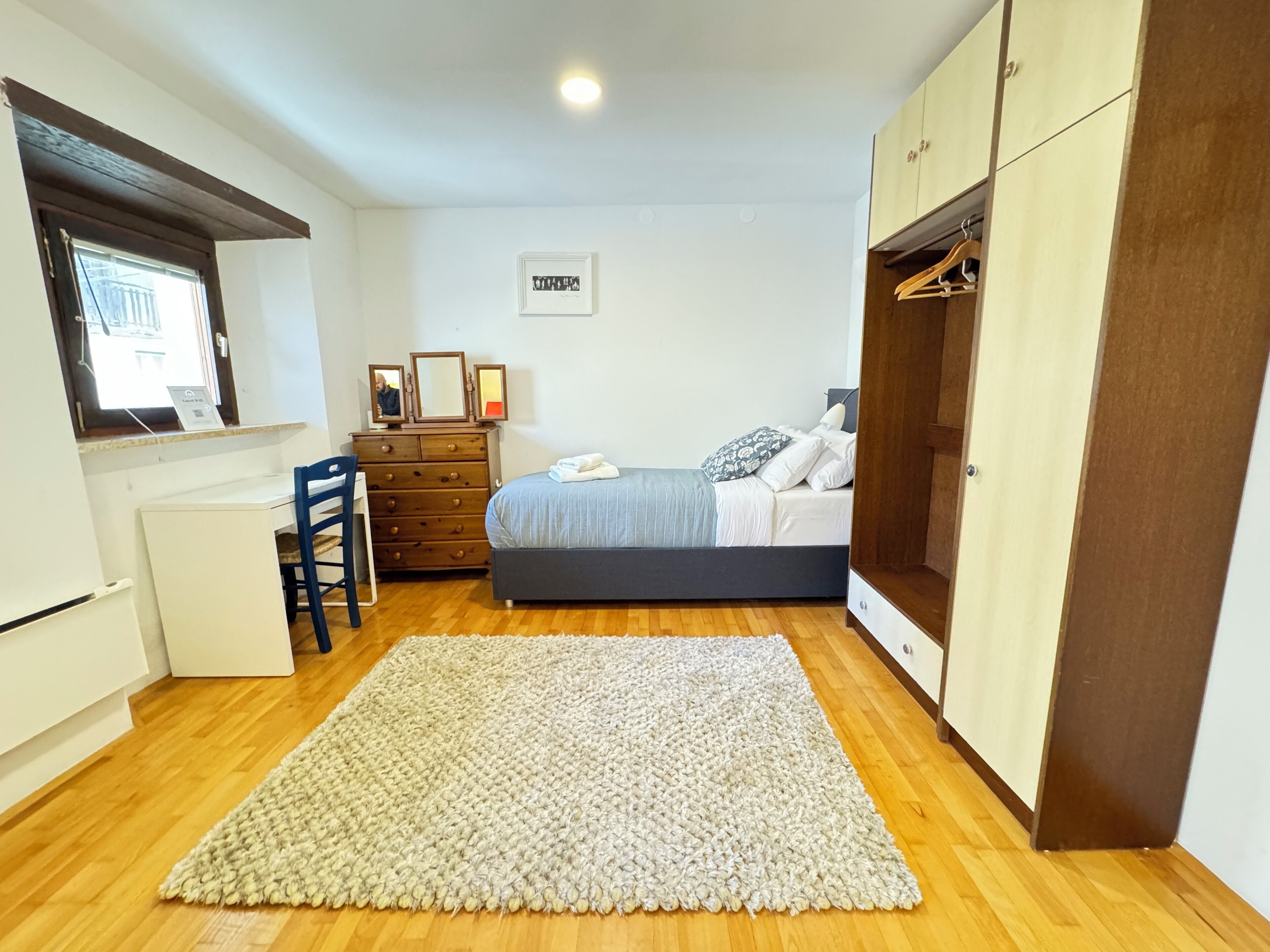 A bedroom with a bed, dresser, desk, chair, and wardrobe.