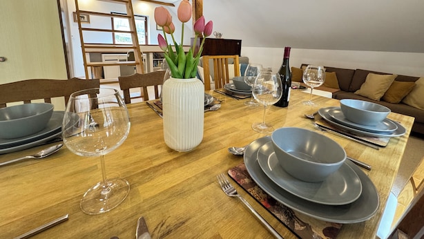 Une table à manger dressée avec des assiettes, des bols, des verres à vin et un vase rempli de fleurs.