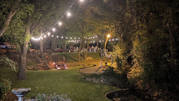 Un espace extérieur aménagé en jardin, avec des guirlandes lumineuses, un escalier en pierre et un coin repas doté de tables et de chaises.
