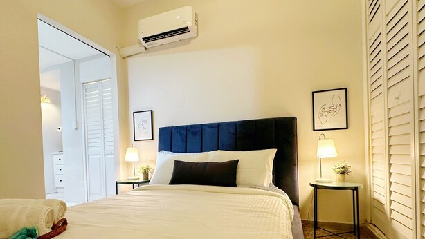 A hotel room with a bed, bedside tables, an air conditioning unit, and a door leading to another room. - Jetsetter's Retreat (Carolina)