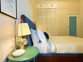 Un dormitorio con cama, mesita de noche con lámpara, planta en maceta y armario.
