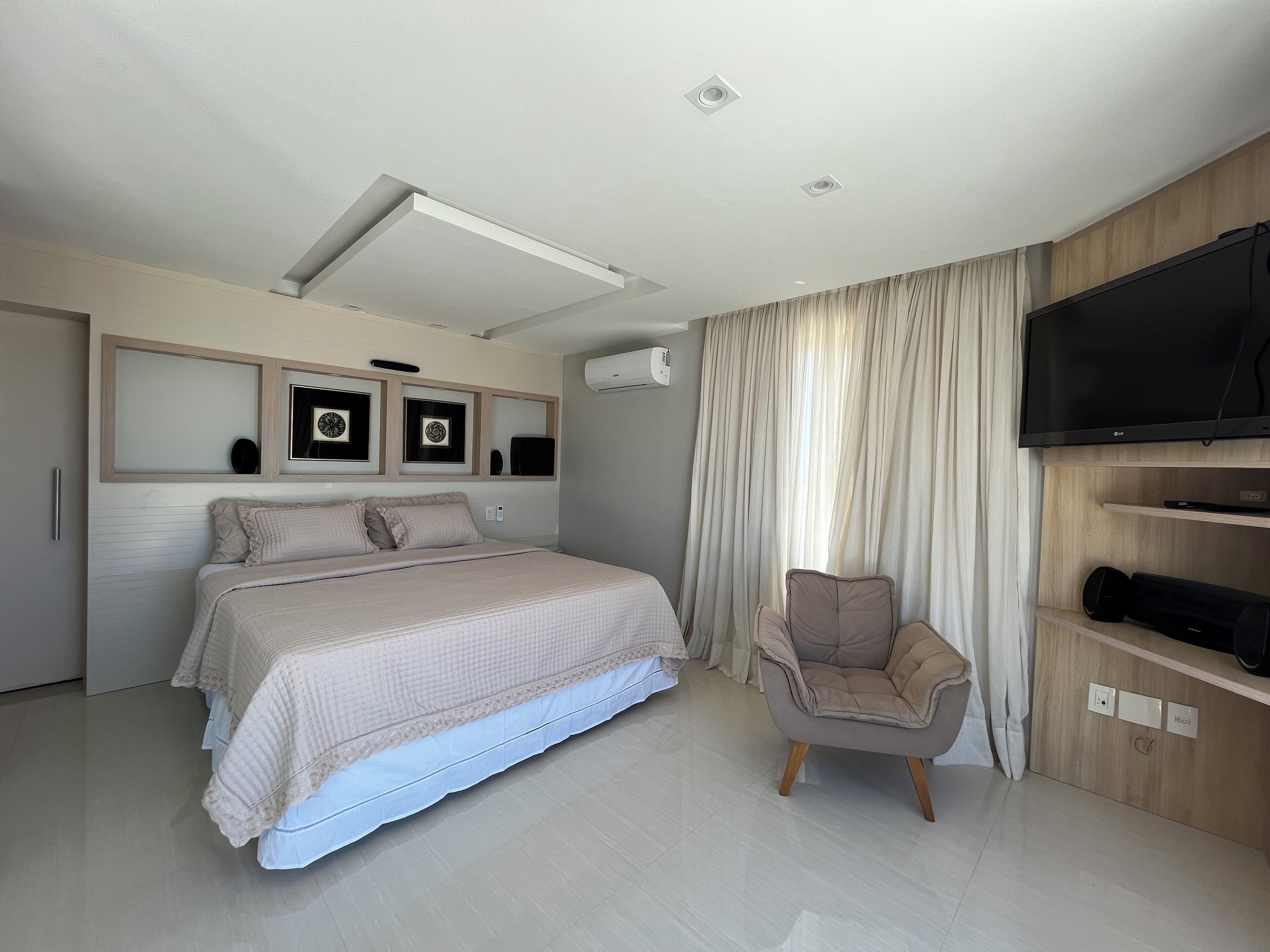 A modern bedroom with a large bed, a TV, and a chair.