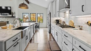 A modern kitchen with white cabinets, a large island, stainless steel appliances, and a herringbone tile backsplash.