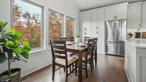 A modern kitchen with white cabinets, a stainless steel refrigerator, and a dining table with chairs.