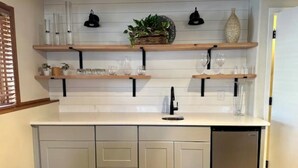 A kitchen with light gray cabinets, a stainless steel dishwasher, and two wooden shelves above the countertop. - Modern Comforts - Stay/Work/Play (Casper)
