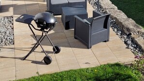 Eine Terrasse im Freien mit Sitzgelegenheit, Grill und einem leuchtend gelben Sonnenschirm.