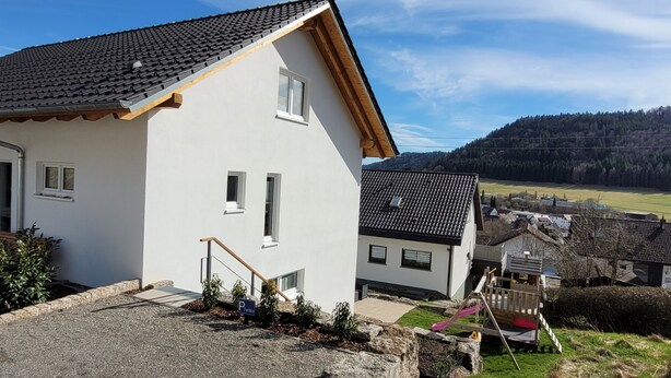 Ein weißes Haus mit einem Ziegeldach, einem kleinen Garten und einem Spielplatz.