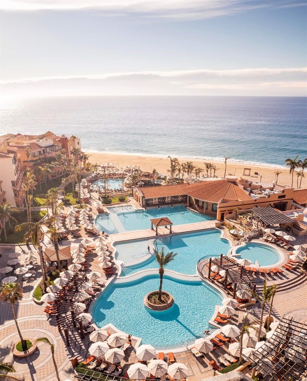 Ein Resort mit mehreren Schwimmbecken, Zugang zum Strand und Palmen.