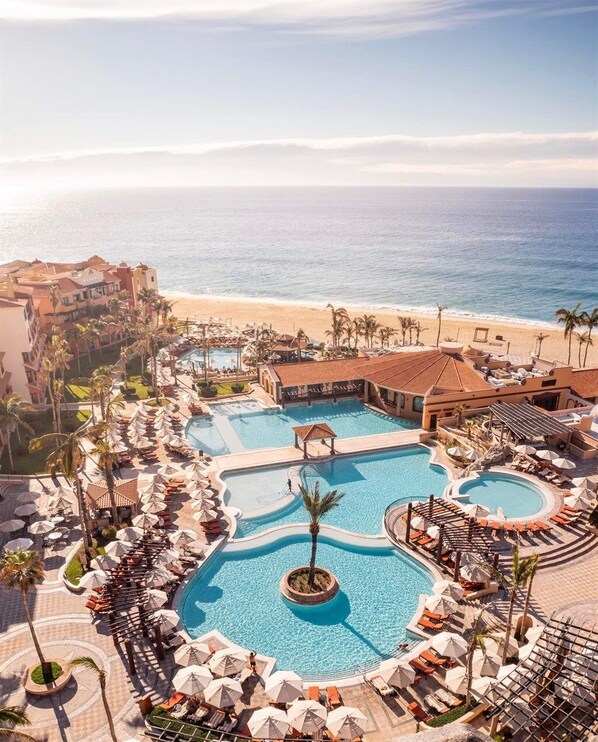 A resort with multiple swimming pools, beach access, and palm trees.
