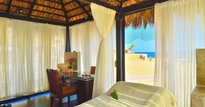 A room with a bed, a table with a vase of flowers, and a view of the beach.