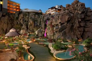 A resort with multiple swimming pools, a waterfall, and a thatched-roof hut.