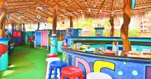 A colorful play area with a thatched roof, a counter with children's toys, and stools.