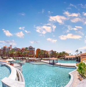 A resort with multiple swimming pools, palm trees, and a clear blue sky.