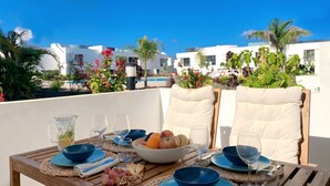 A dining table set with blue plates, glasses, and a bowl of fruit and nuts, overlooking a pool and white buildings.