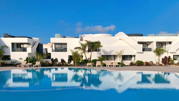A modern hotel with a swimming pool, white buildings, and palm trees.