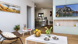 A modern living room with a dining area, a kitchen, and a TV displaying a scenic view. - Charming 3BR Villa for 6, With Heated Pool with Waterfall (Omiš)