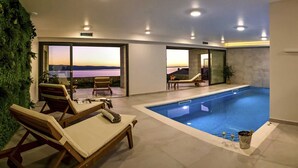 A modern indoor swimming pool with lounge chairs and a view of the sunset. - Charming 3BR Villa for 6, With Heated Pool with Waterfall (Omiš)
