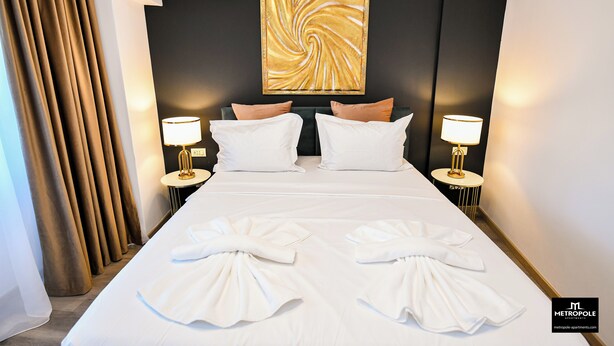 A hotel room with a large bed, two bedside lamps, a wall-mounted air conditioner, and a decorative swirl painting. - Metropole Apartments Central City (Bucharest)