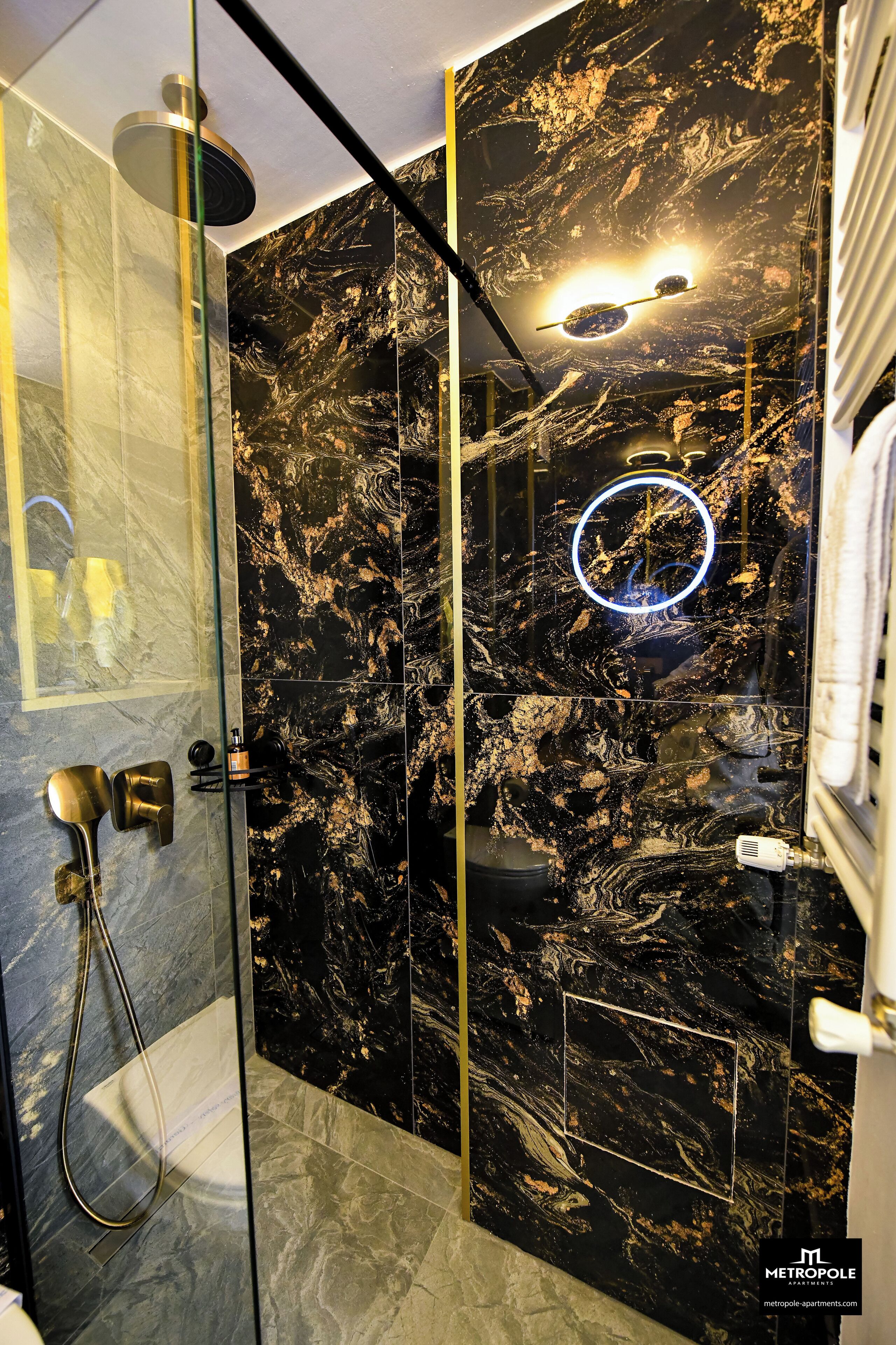 A modern bathroom with a glass-enclosed shower, marble walls, and a circular light fixture.