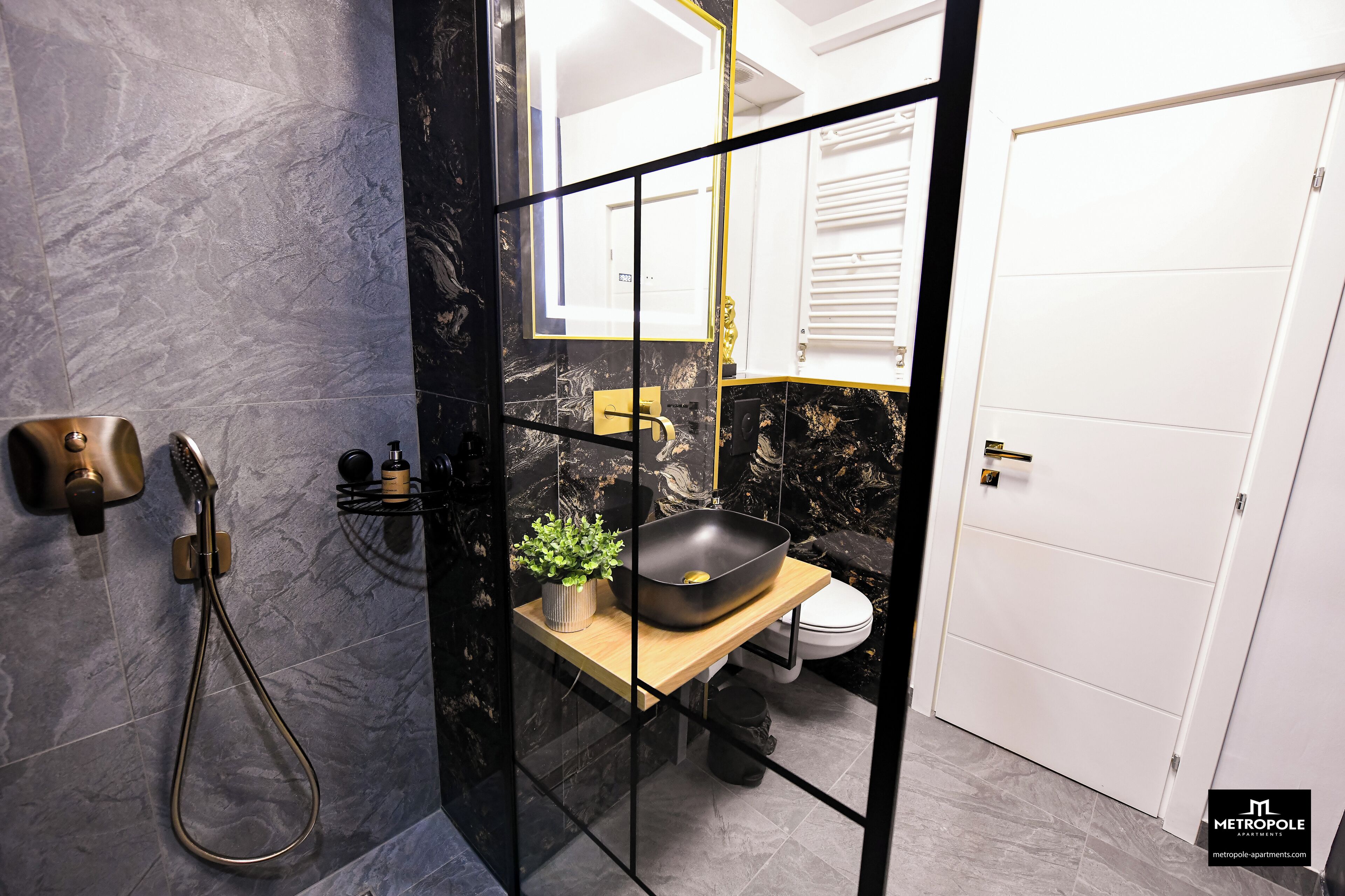 A modern bathroom with a black and gold color scheme, featuring a shower, sink, and toilet.