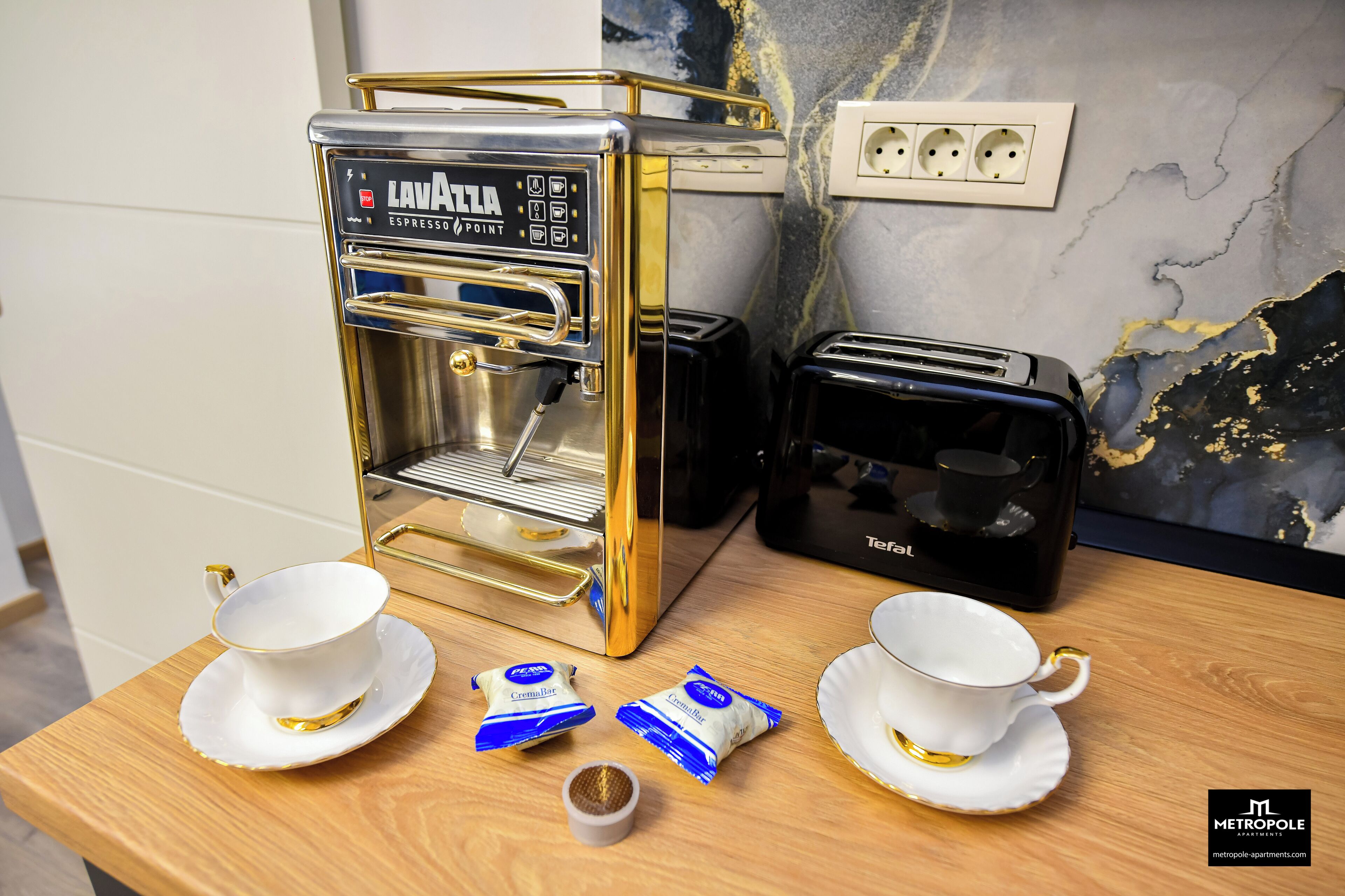 A coffee machine, two cups, and two packets of creamer on a wooden table.