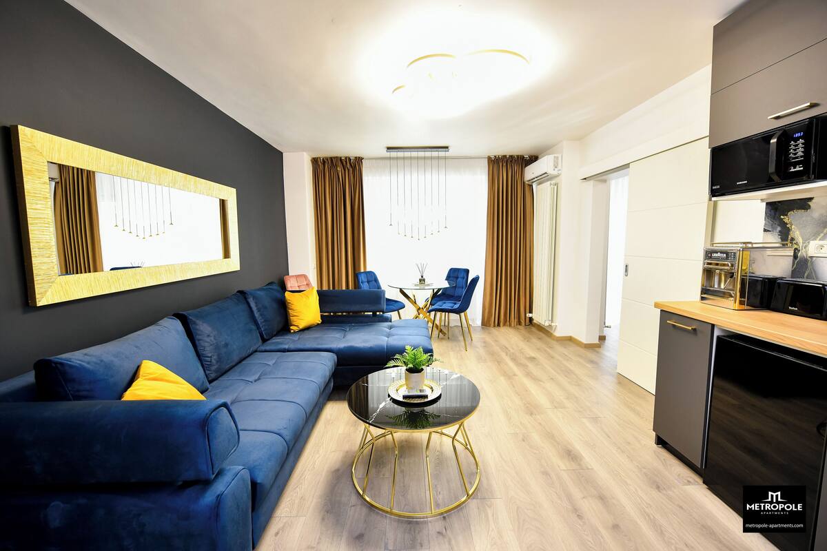A modern living room with a blue sofa, a round coffee table, and a kitchen area with a microwave.