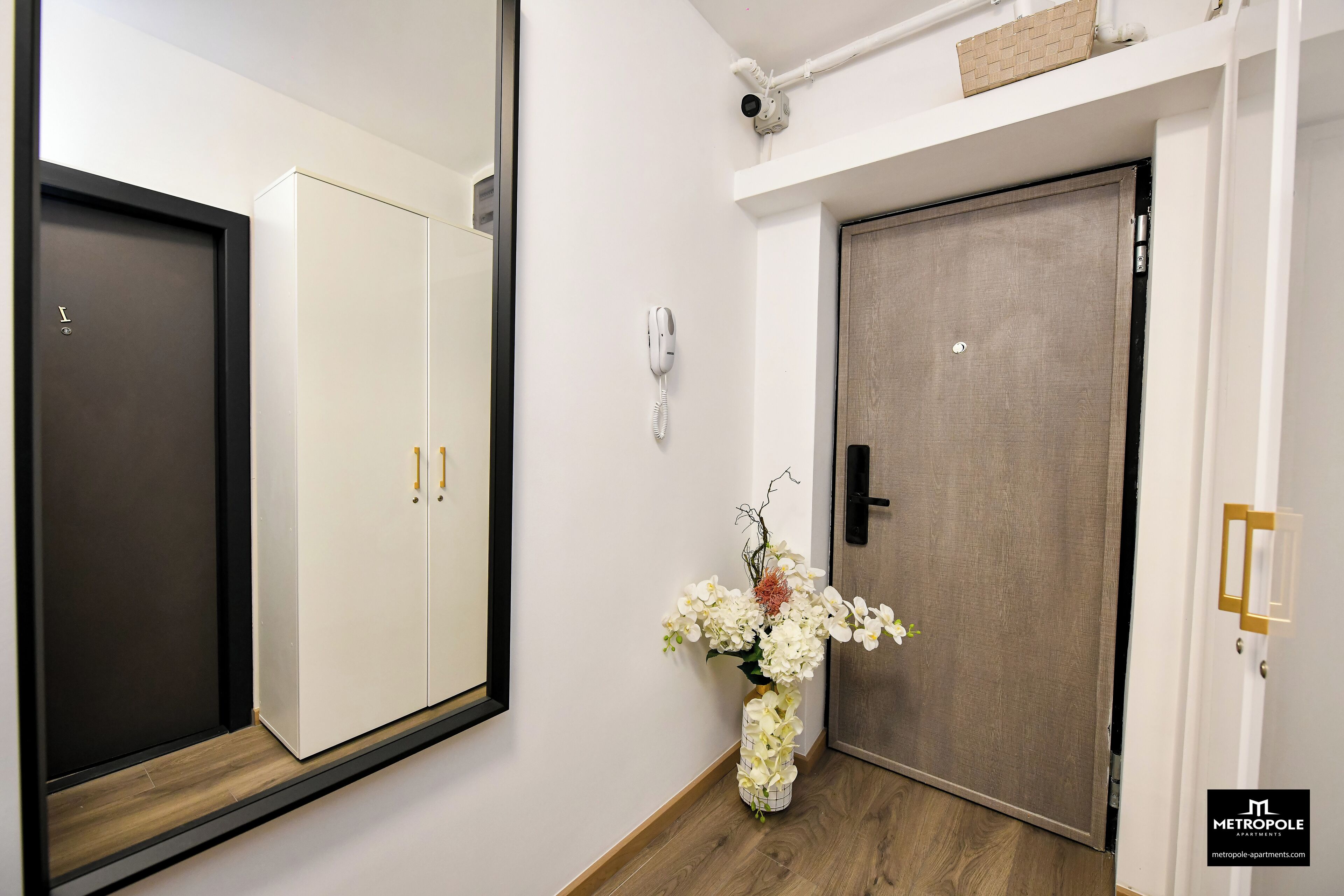 A hallway with a wardrobe, a door, a security camera, a phone, and a vase with flowers.