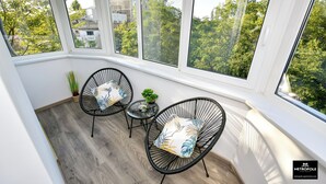 A sunlit room with large windows, two black wire-framed chairs with patterned cushions, a small round table, and a potted plant. - Metropole Apartments Central City (Bucharest)