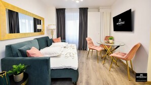 A modern hotel room with a bed, a glass table with chairs, a TV, and a large mirror. - Metropole Apartments Central City (Bucharest)