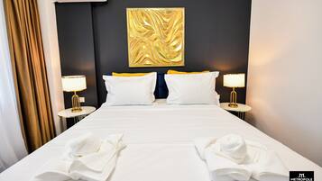A hotel room with a large bed, two bedside tables with lamps, a gold abstract artwork on the wall, and a dark accent wall.