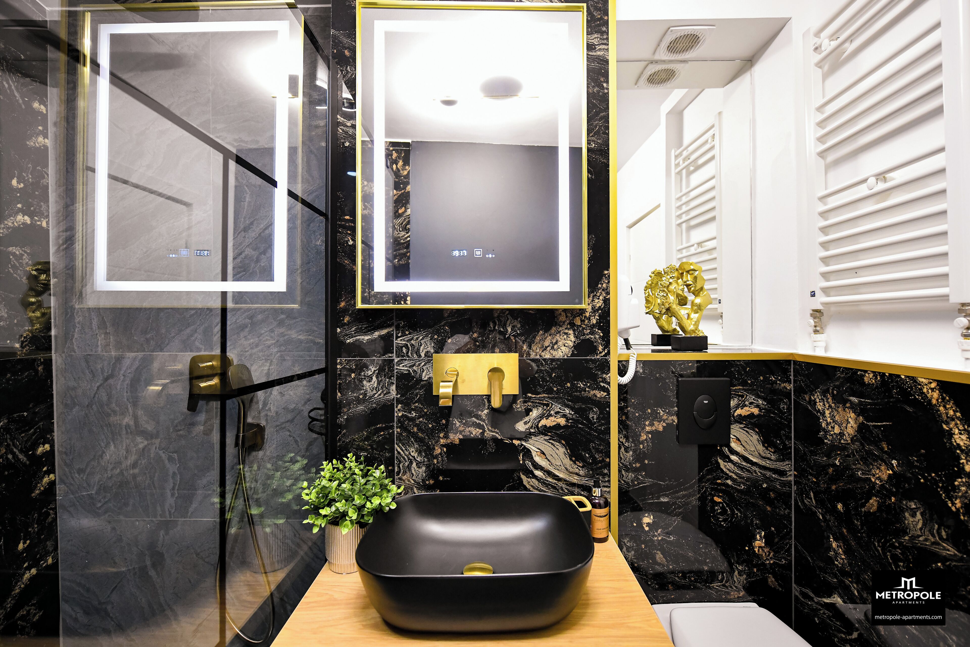 Um banheiro moderno com uma pia de mármore preto, detalhes dourados e um espelho grande.