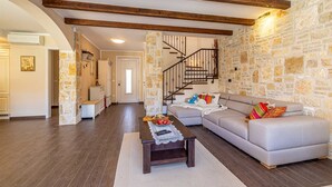 Un salon avec un mur en pierre, un canapé gris, une table basse en bois et un escalier avec une rampe en bois.