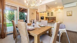 Un coin repas avec une table en bois, des chaises en osier, un lustre et une vue sur l’extérieur.