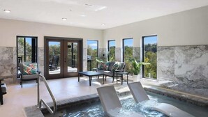 Un área de piscina interior moderna con sillones de descanso, una zona de estar y amplias ventanas con vistas al exterior.