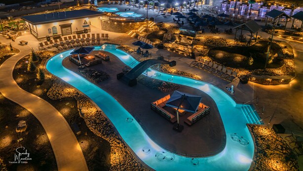 Vista nocturna de un resort con múltiples piscinas, zonas de descanso y mobiliario exterior.