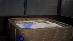 Ein Whirlpool auf einer Holzdielen-Terrasse, im Hintergrund Metallpaneele und Beleuchtung.
