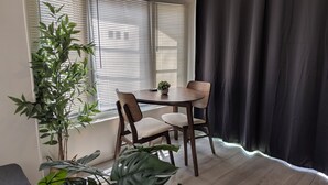 Ein Zimmer mit einem runden Holztisch, zwei Stühlen, einem Blumentopf und einem Fenster mit Jalousien.