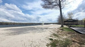 Une plage de sable avec un poste de surveillance pour les sauveteurs, un pavillon abrité et une zone herbeuse avec des arbres.