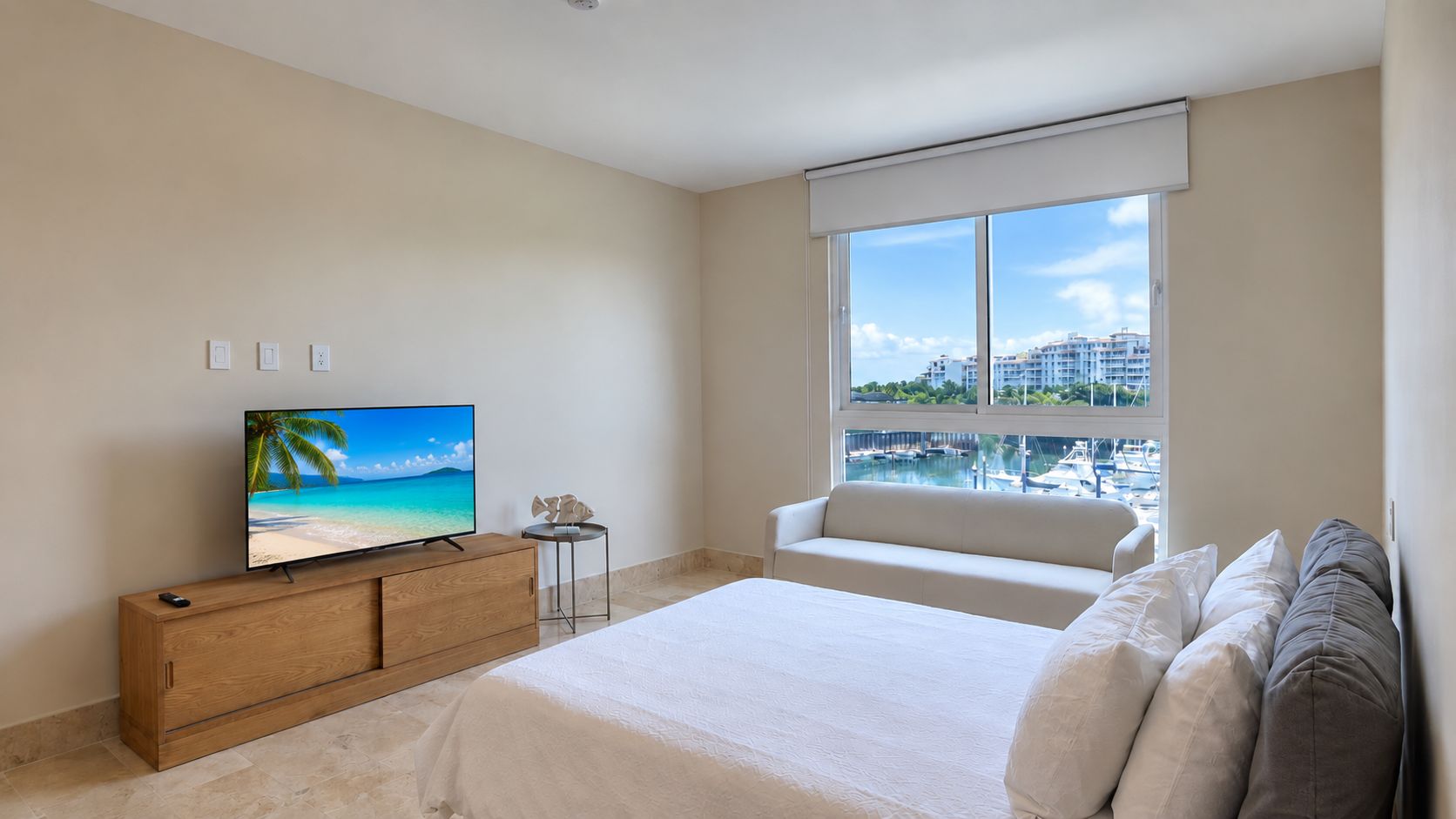 Una habitación de hotel con una cama, televisión, una mesita y ventana con vista al puerto deportivo.
