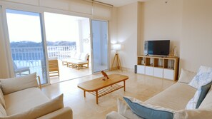 Un salón amplio con balcón, televisor y una mesa de centro de madera.
