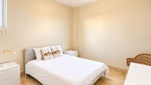 A bedroom with a bed, two bedside lamps, a nightstand, a chair, and a wall-mounted light switch.