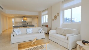 A modern living room with a sofa, a coffee table, and a view of the kitchen in the background.