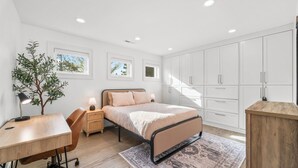 A bedroom with a bed, nightstands, a desk, a large wardrobe, and a potted plant.