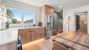 A modern kitchen with a stainless steel refrigerator, wooden cabinets, a large island with a sink, and a dining area with a wooden table and chairs.