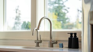 A kitchen sink with a modern faucet, a soap dispenser, and a window with a view of trees.