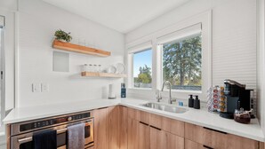 A modern kitchen with white cabinetry, a built-in oven, a sink, and a window with a view of trees.