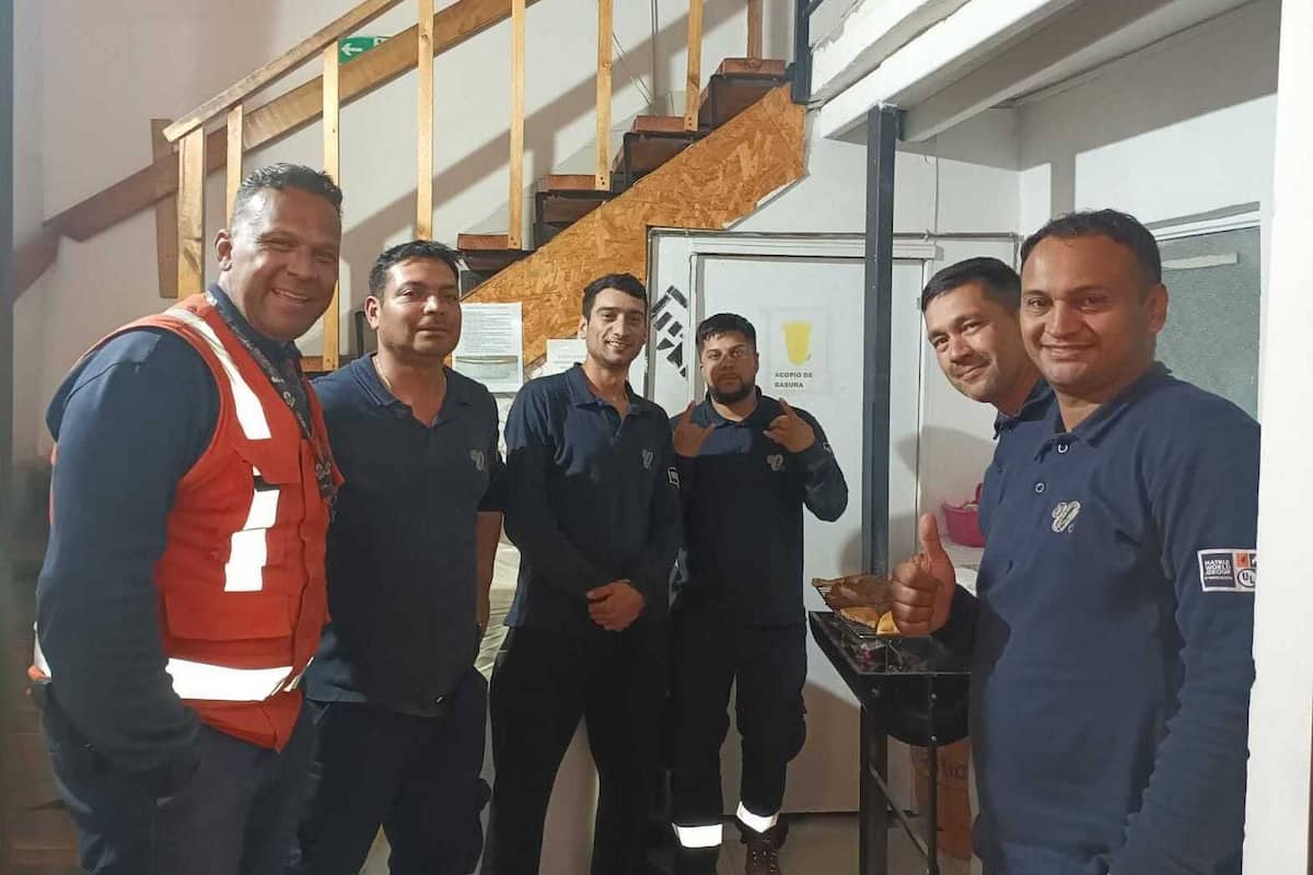 Un groupe d’hommes se trouve dans une pièce où il y a un escalier et une porte sur laquelle est inscrit « DÉCHETS ».