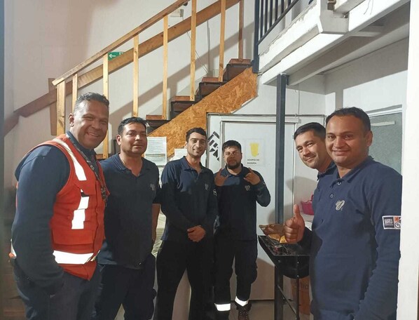 A group of men in a room with a staircase and a door labeled "ACOPIO DE BASURA". - Pampaloja (Antofagasta)